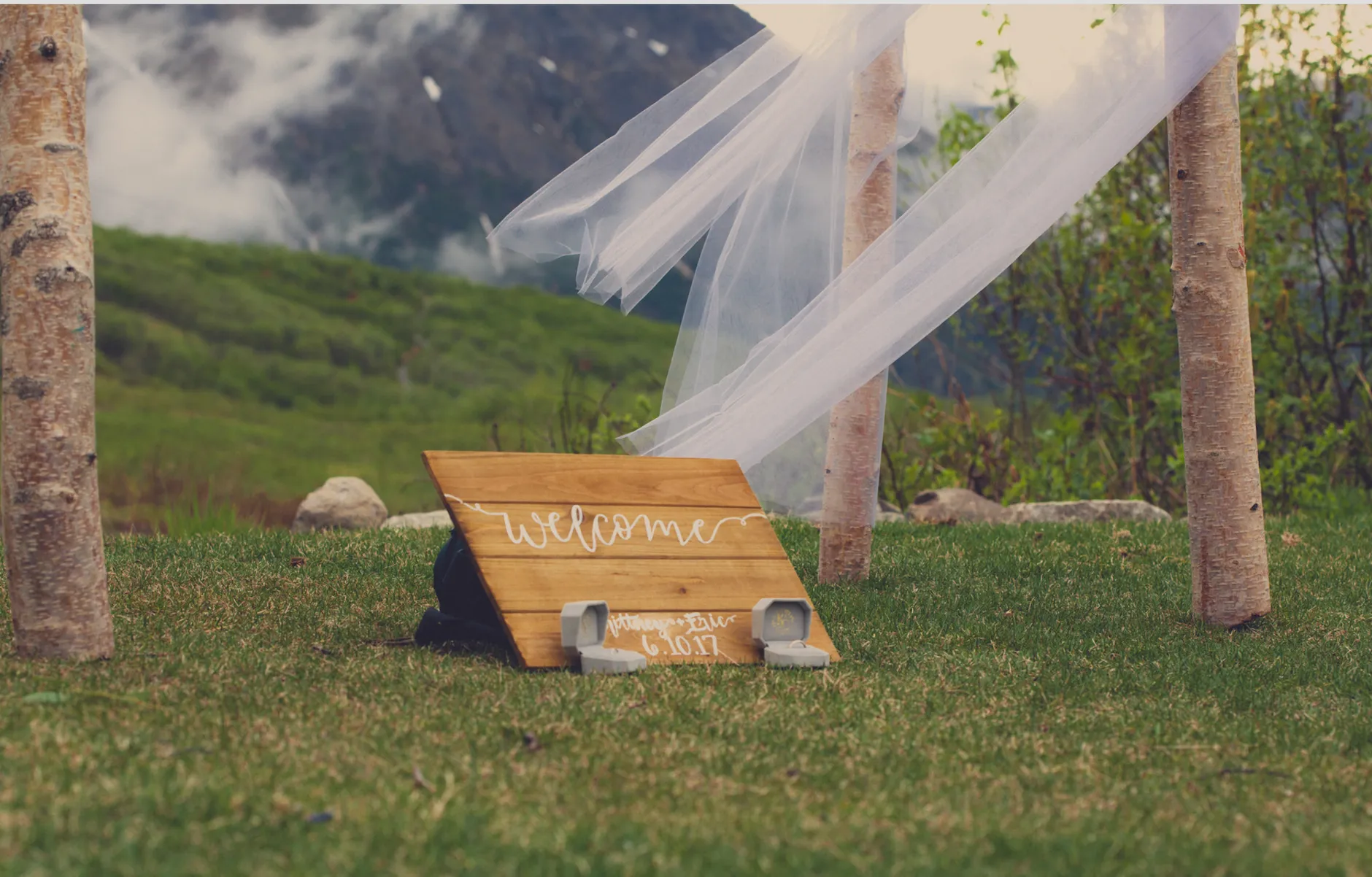 Charming outdoor wedding scene with welcome sign, delicate veil, and picturesque mountain backdrop in Kenai, Alaska.